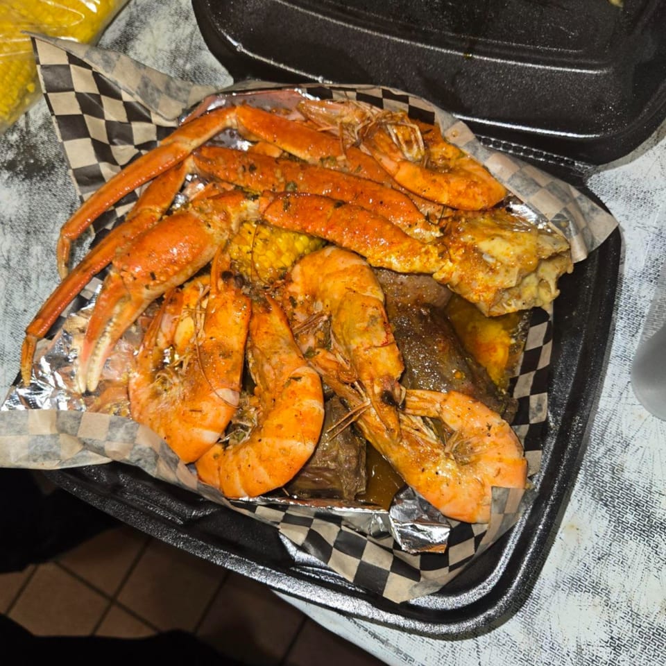 A takeout container filled with seasoned shrimp, crab legs, corn on the cob, and other seafood.
