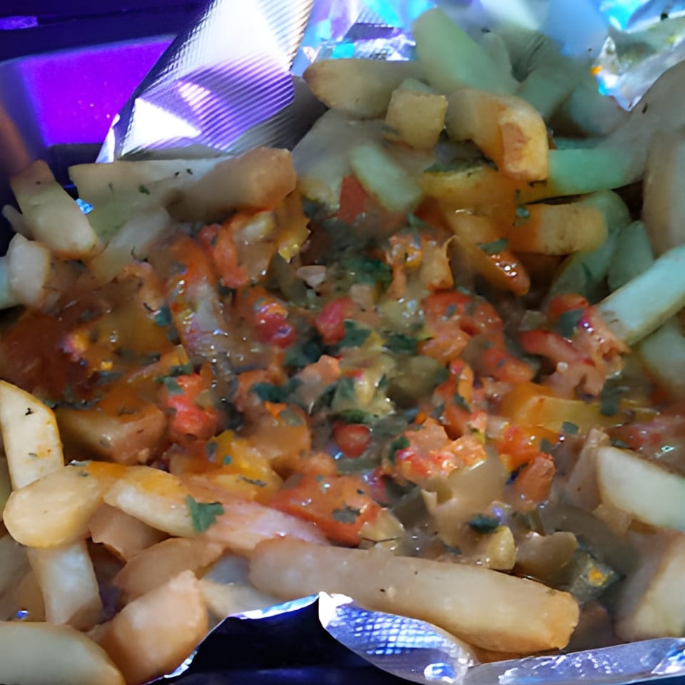 Close-up of golden french fries topped with a savory sauce, diced tomatoes, and herbs.