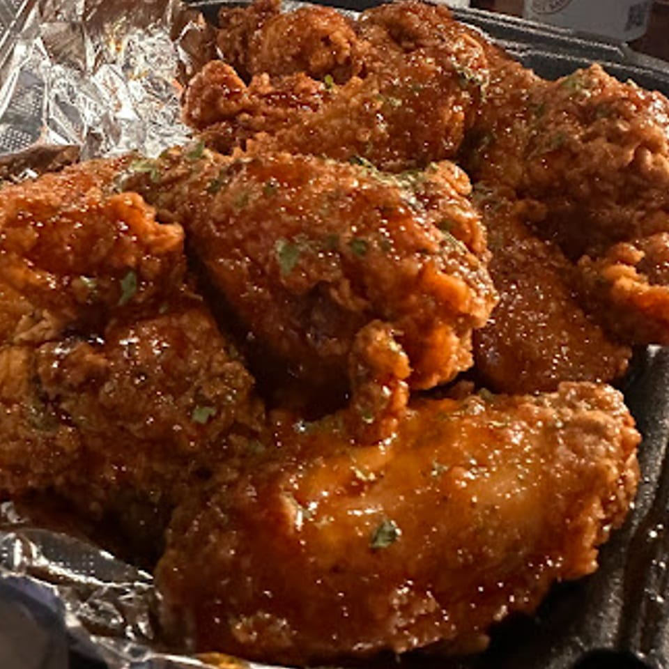 Close-up of crispy, glazed Bourbon Square Jazz Bar chicken wings with herbs in a foil-lined container.