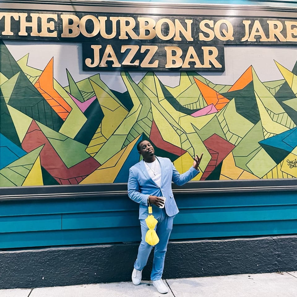 Man in a light blue suit posing in front of The Bourbon Square Jazz Bar's colorful mural.