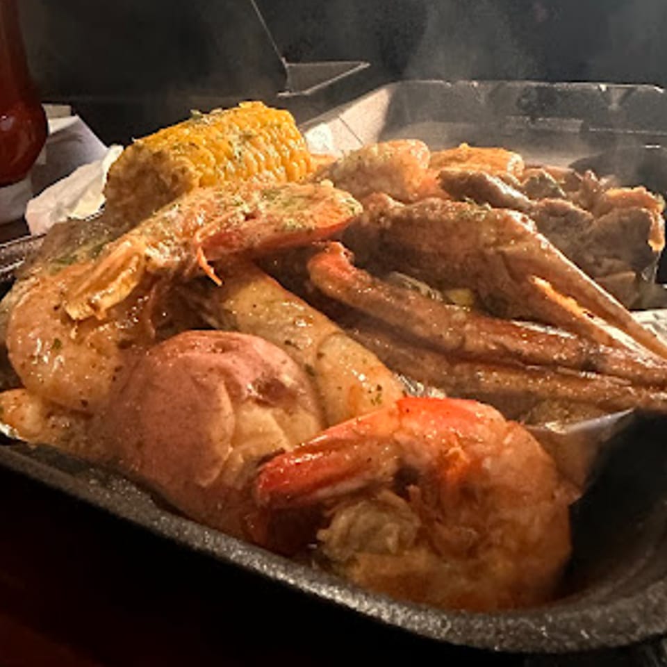 Steaming seafood boil with shrimp, crab legs, potatoes, and corn on the cob.